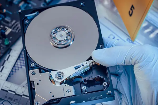 Técnico com luvas manipulando um HD aberto em ambiente de laboratório